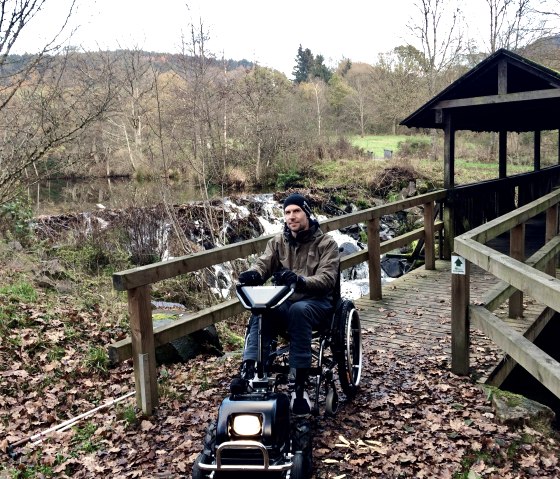 Dr. Holger Tülp testet ein Gespann aus Rollstuhl und Zuggerät auf dem zertifizierten barrierefreien Komfort-Weg rund um den Stausee Irrhausen. , © Naturpark Südeifel/Dr. Holger Tülp